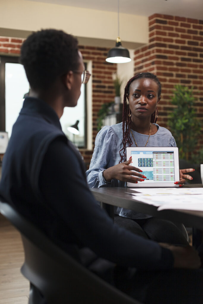african american business woman presenting to coworker accounting documentation statistics data on tablet.